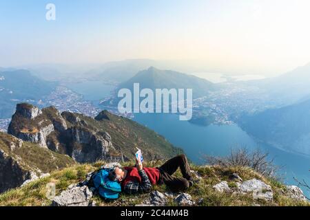 Rückansicht eines Wanderers, der ein Buch über Berggipfel, Orobie Alps, Lecco, Italien liest Stockfoto