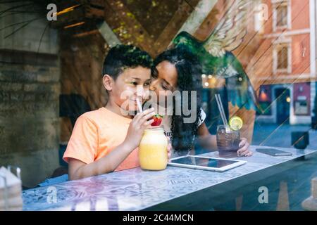 Junge Frau küssen Sohn trinken Smoothie durch Restaurant Fenster gesehen Stockfoto