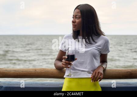 Porträt einer jungen Frau mit einem Glas Rotwein vor dem Meer Stockfoto