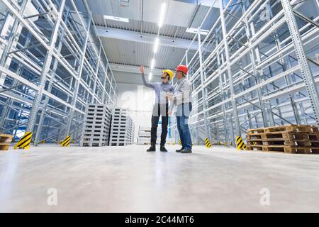 Zwei Männer mit Schutzmützen reden im Lagerhaus einer Fabrik Stockfoto