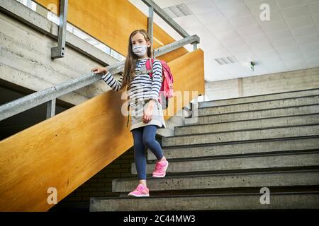 Mädchen trägt Maske in der Schule zu Fuß die Treppe hinunter Stockfoto