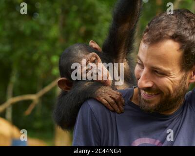 Kamerun, Ponysongo, lächelnder Mann mit Schimpansen (Pan troglodytes) auf dem Rücken Stockfoto