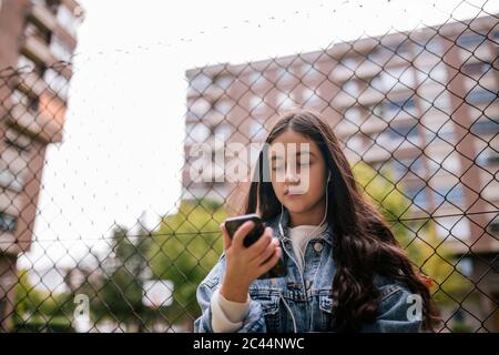 Low-Angle-Ansicht von Teenager-Mädchen mit Smartphone, während sie gegen Kettengliederzaun stehen Stockfoto