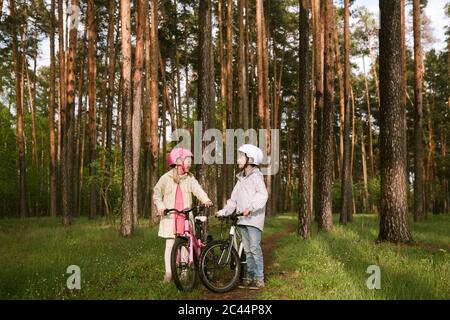 Mädchen und Junge stehen mit Fahrrädern im Wald Stockfoto