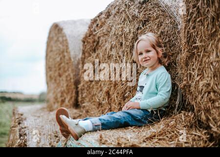 Portrait von lächelndem Mädchen auf Strohballen sitzend Stockfoto