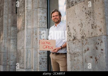 Lächelnder Ladenbesitzer hält Pappe mit Eröffnungsansage in der Stadt Stockfoto