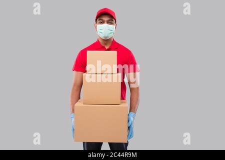 Lieferung Mann Holding Karton Boxen Tragen von medizinischen Maske und Handschuhe isoliert. Indian Delivery Boy lächelnd mit Boxen in den Händen Stockfoto