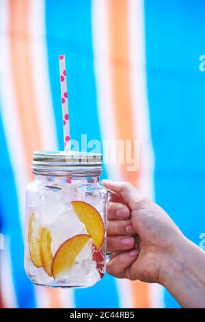 Nahaufnahme einer Hand, die Trinken der Frau im Marmeladenglas gefüllt mit Eis und Scheiben von Pfirsich Stockfoto