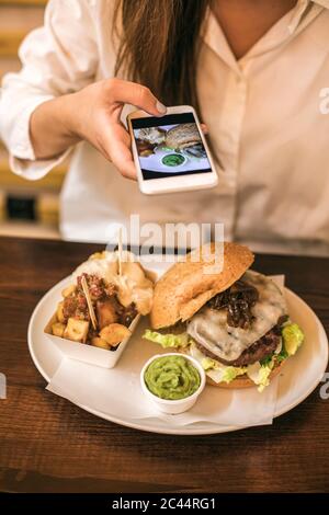 Mittelteil der Frau fotografieren frische Mahlzeit serviert in der Platte auf dem Tisch im Restaurant Stockfoto