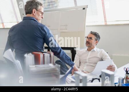 Reife Geschäftsleute diskutieren über Dokument, während im Büro sitzen Stockfoto