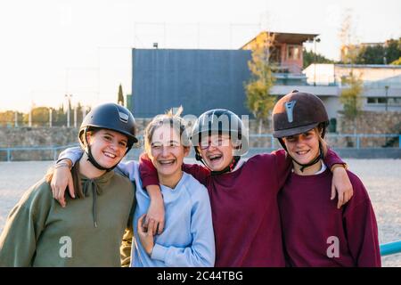 Porträt von fröhlichen weiblichen Jockeys, die an sonnigen Tagen gemeinsam gegen den Trainingsboden stehen Stockfoto