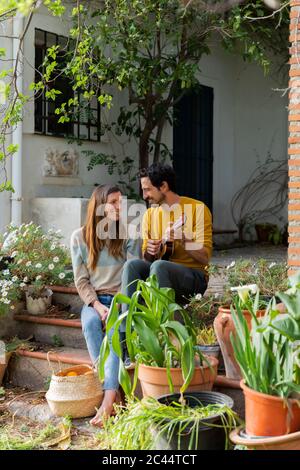 Mann spielt Gitarre, während er mit Freundin auf Stufen des Bauernhauses sitzt Stockfoto
