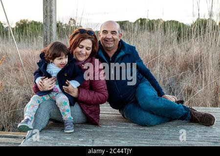 Lächelnde Großeltern mit Enkelin auf dem Boden sitzen auf dem Land Stockfoto