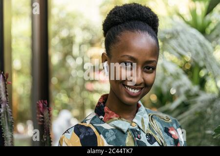 Porträt einer lächelnden jungen Frau, die im Garten Musik mit Ohrhörern hört Stockfoto
