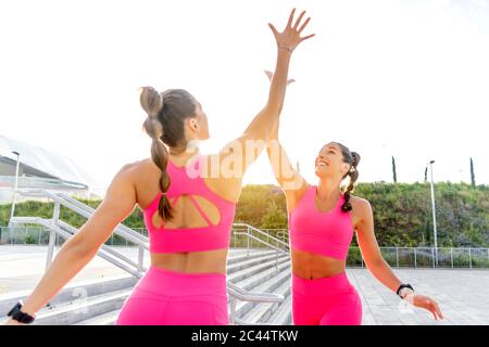 Glückliche junge Zwillingsschwestern geben High-fünf gegen klaren Himmel Stockfoto