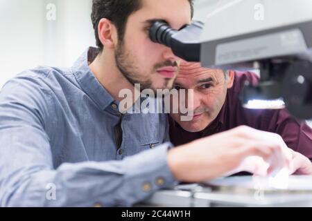 Mann, der in einer Fabrik durch das Mikroskop schaut Stockfoto