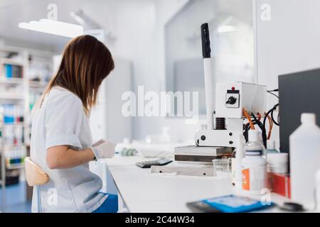 Seitenansicht einer Ärztin mit langen braunen Haaren, die während der Arbeit im Labor am Schreibtisch sitzt Stockfoto