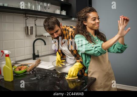 Junge multiethnische Paare putzt ihre Küche. Die Frau ist faul und der Mann ist wütend. Stockfoto