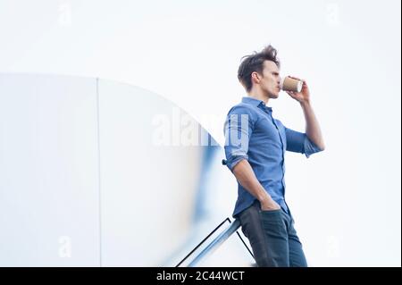 Nachdenklicher Geschäftsmann trinkt Kaffee, während er gegen den klaren Himmel steht Stockfoto