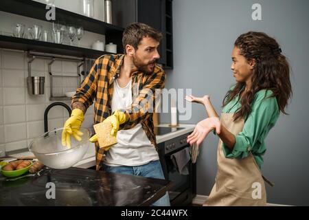 Junge multiethnische Paare putzt ihre Küche. Die Frau ist faul und der Mann ist wütend. Stockfoto