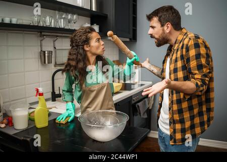 Junge multiethnische Paare putzt ihre Küche. Sie streiten sich. Stockfoto