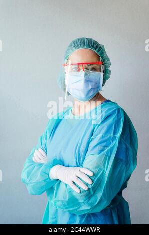 Selbstbewusste weibliche Zahnärztin trägt schützende medizinische Peelings, während sie mit gekreuzten Armen an der Wand in der Klinik steht Stockfoto