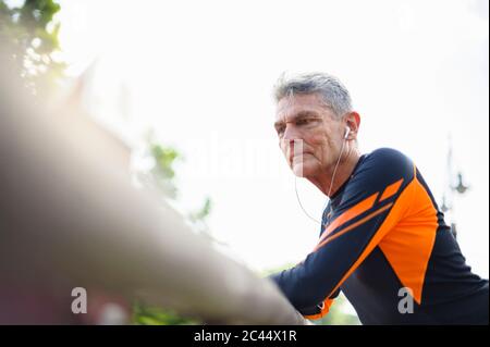 Aus der unteren Perspektive sehen Sie einen müden älteren Mann, der sich am Geländer stützt und über Kopfhörer hört Stockfoto