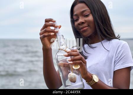 Porträt einer jungen Frau vor dem Meer, die in einer Flasche Nachricht sendet Stockfoto