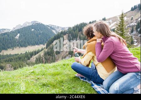 Glückliche Frau, die sich auf den Mann lehnt, der während des Picknicks auf dem Berg eine Champagnerflasche öffnet Stockfoto