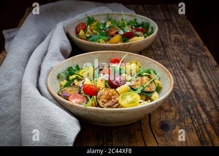 Zwei Schüsseln Pasta-Salat mit gegrillten Zucchini, Tomaten, Rucola, spanische Zwiebel und Balsamico-Essig Stockfoto