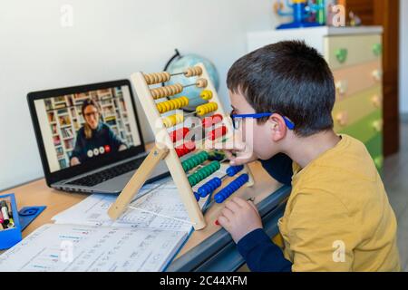 Junge mit Abakus am Schreibtisch während Lehrer auf Video-Anruf während Pandemie homeschooling Stockfoto