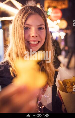 Portrait von lächelnd blonde Mädchen essen Kartoffel Chip an Karneval in der Stadt während der Nacht. München, Deutschland Stockfoto