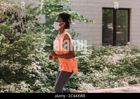 Sportliche junge Frau mit Schutzmaske läuft Stockfoto