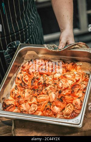 Junger männlicher Koch hält gebackene Tomaten in Backblech im Restaurant Stockfoto