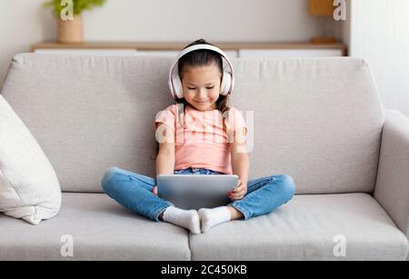 Asiatische Mädchen Mit Tablet-Computer Tragen Von Kabellosen Kopfhörern Zu Hause Stockfoto