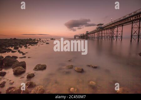 Llandudno Pier bei Sonnenuntergang mit einem glatten Meer und Felsen. Touristenziel Stockfoto