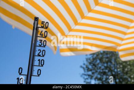 Thermometer zeigt über dreißig Grad celsius mit gelb gestreiftem Sonnenschirm und blauem Himmel Stockfoto