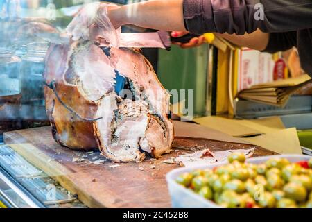 Das traditionelle Schweinefleisch von Ariccia auf dem Tresen eines Straßenverkäufers (italienisches Essen). Eine Frau schneidet das Schweinefleisch, um ein Sandwich zu machen. Frascati, Ariccia, Rom, Stockfoto