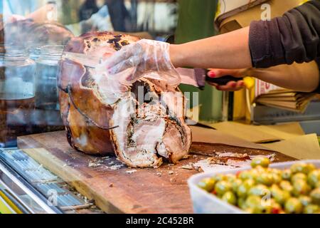 Das traditionelle Schweinefleisch von Ariccia auf dem Tresen eines Straßenverkäufers (italienisches Essen). Eine Frau schneidet das Schweinefleisch, um ein Sandwich zu machen. Frascati, Ariccia, Rom, Stockfoto