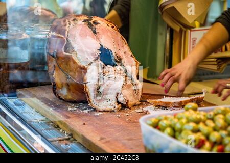 Das traditionelle Schweinefleisch von Ariccia auf dem Tresen eines Straßenverkäufers (italienisches Essen). Eine Frau schneidet das Schweinefleisch, um ein Sandwich zu machen. Frascati, Ariccia, Rom, Stockfoto