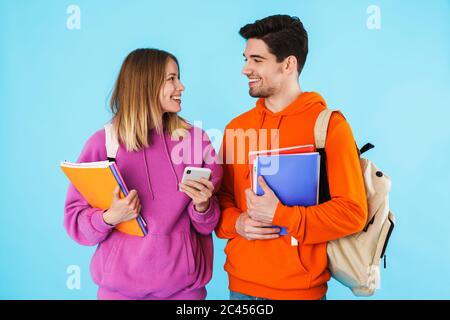 Porträt eines fröhlichen jungen Studenten in Rucksäcken, die Lehrbücher tragen, die isoliert auf blauem Hintergrund stehen Stockfoto