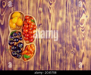 Gruppe von frischen Tomaten. Tomaten in verschiedenen Farben und Arten in einer Holzschale Stockfoto