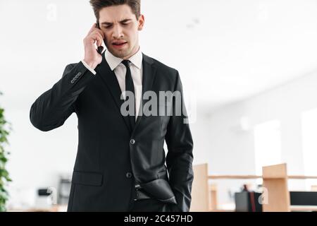 Bild von unzufrieden jungen Geschäftsmann in schwarzem Anzug reden auf Handy im Büro Stockfoto