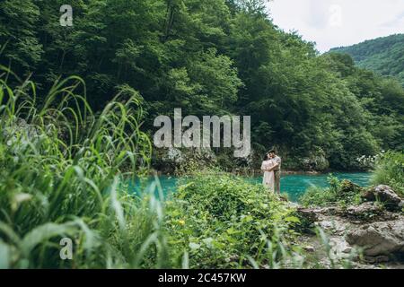 Junges Paar in der Natur. Ein Mann umarmt eine Frau auf einem Hintergrund mit einem schönen Blick auf den Fluss. Stockfoto