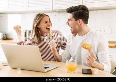 Porträt des aufgeregt Paar mit Laptop und Kreditkarte, während die Gewinner Geste in der Küche zu Hause Stockfoto