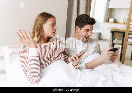 Portrait von schönen emotionalen Paar mit Handys, während im Bett zu Hause liegen Stockfoto