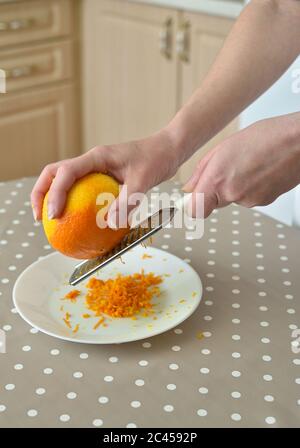 Nahaufnahme einer Frau, die Orangenschale auf der Reibe reibt Stockfoto