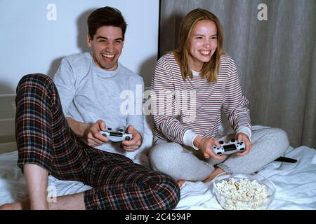 Portrait von aufgeregt niedlichen Paar hält Joysticks während der Wiedergabe von Videospielen im Bett zu Hause Stockfoto