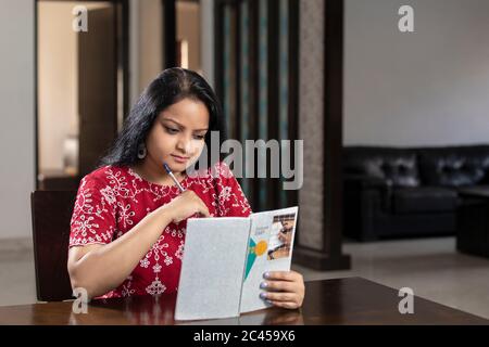 Eine indische Frau schreibt Notizen in ihr Tagebuch, eine asiatische Frau sitzt in ihrem Wohnzimmer und plant in ihrem Tagebuch Stockfoto
