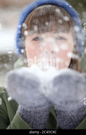 Junge Frau bläst Schnee aus ihrer Hand Stockfoto